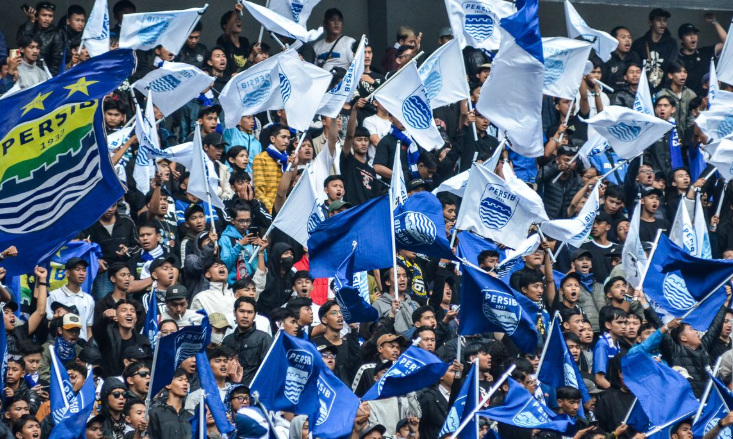 Atmosfer gemuruh kerumunan suporter Persib Bandung (Bobotoh) mengibarkan bendera di tribun stadion.